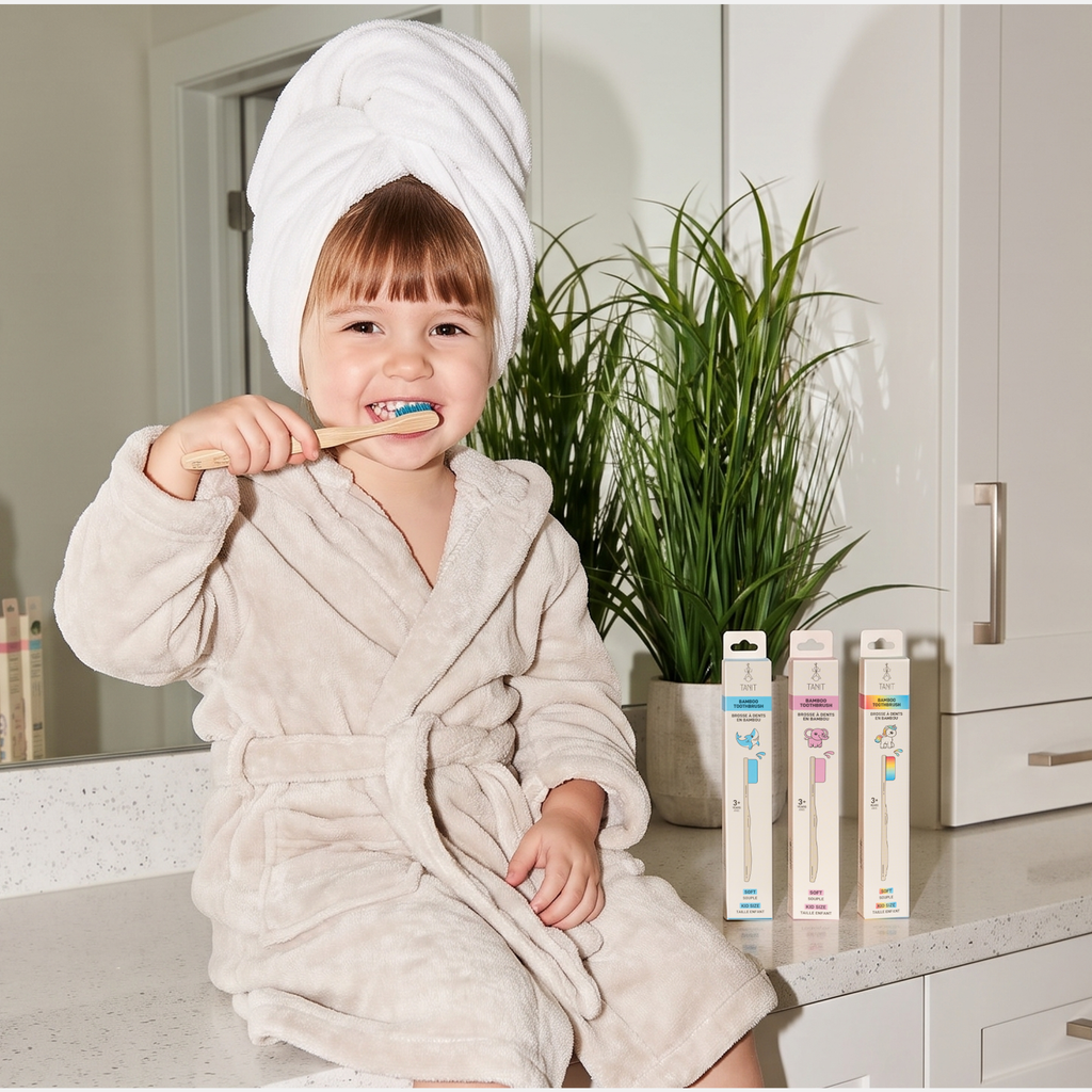 A young child in a bathrobe brushing their teeth with a TANIT kids bamboo toothbrush