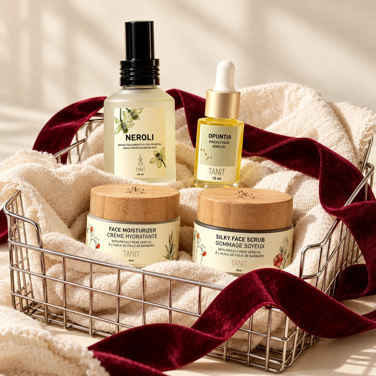 TANIT Neroli skincare essentials in a wire basket with ivory linen and burgundy ribbon